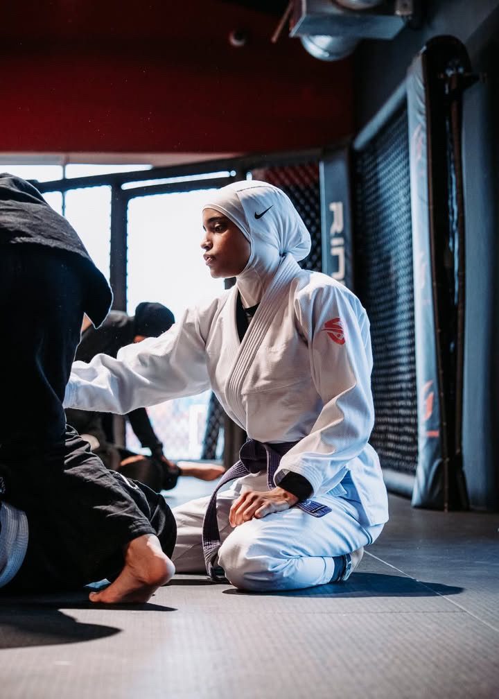 Sana Ndiaye à genoux sur le tapis, en train d'expliquer un mouvement à un partenaire.