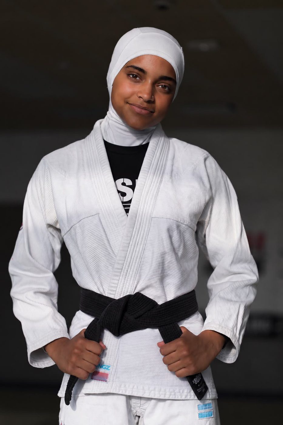 Sana Ndiaye en kimono blanc et hijab blanc, souriante, les mains sur sa ceinture noire.